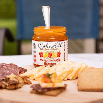 Jar of Blake Hill Mango Pineapple Habanero on a charcuterie board with various foods.
