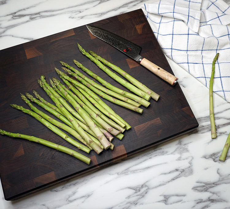 Green asparagus on a Walnut End Grain cutting board with a knife, on a marble surface.