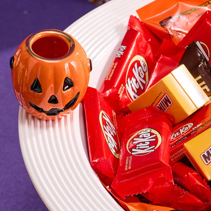 Halloween-themed candy including Kit Kat bars and a small pumpkin-shaped container on a white plate.