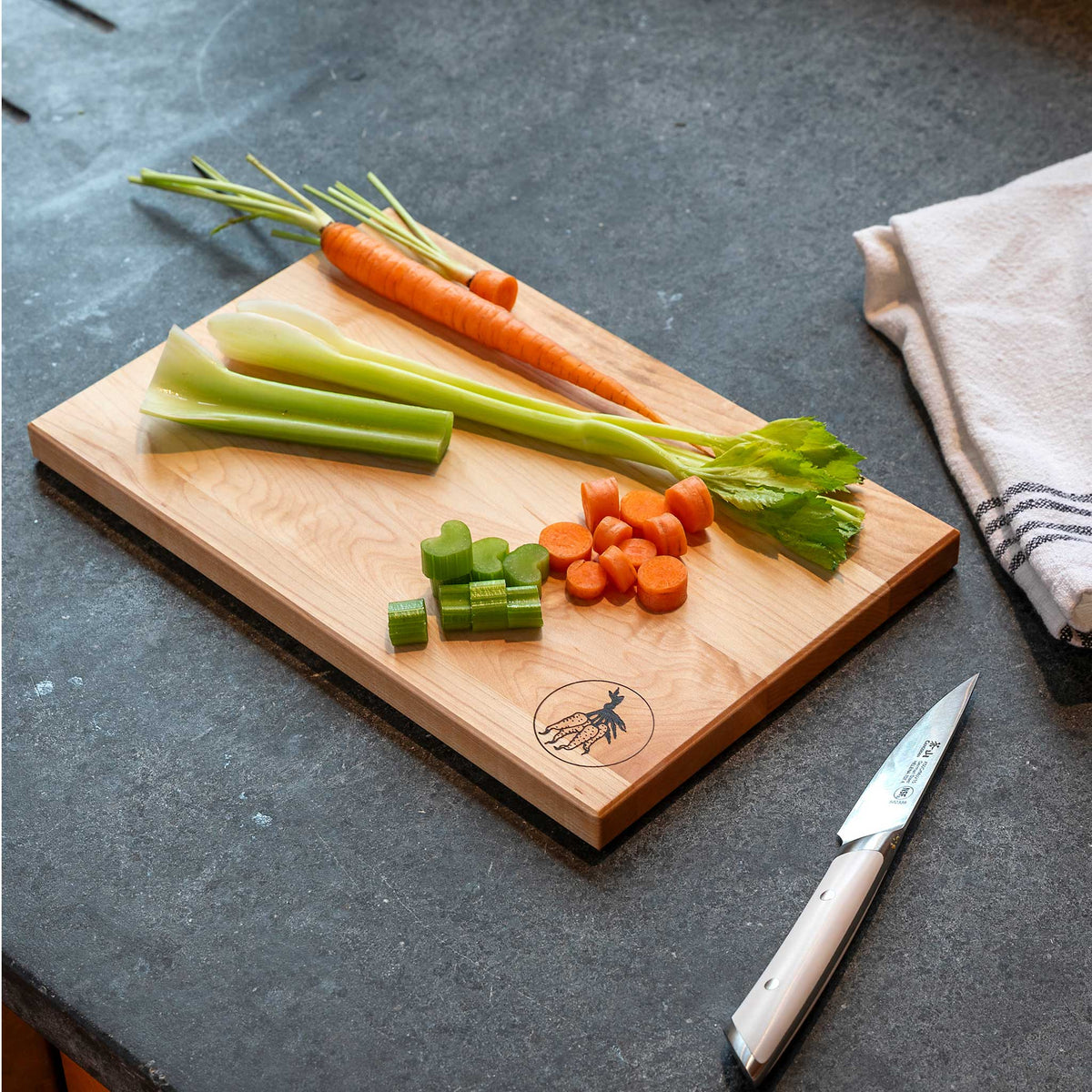 Wooden cutting board with chopped vegetables and a knife on a dark surface