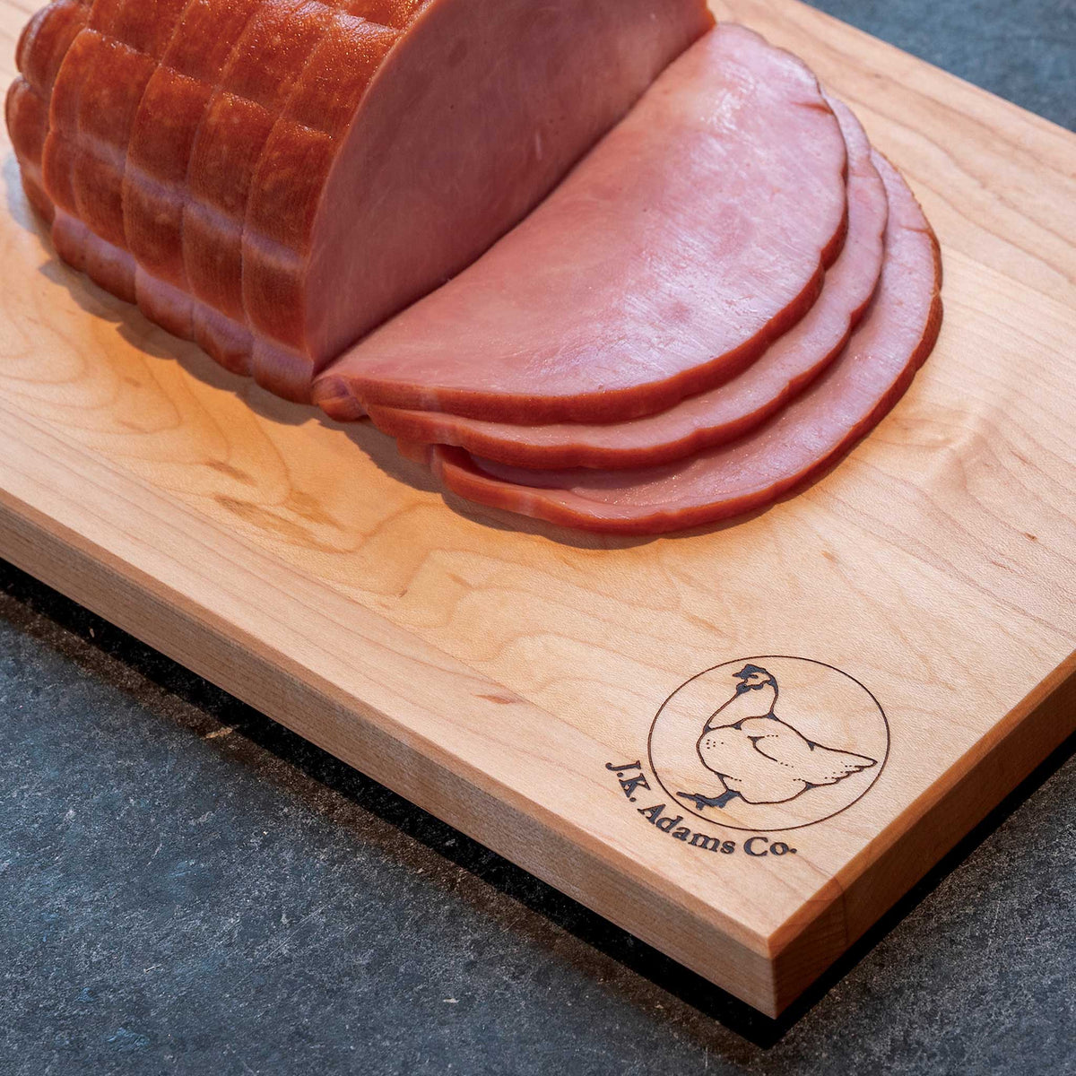 Sliced ham on a wooden cutting board with a brand logo.